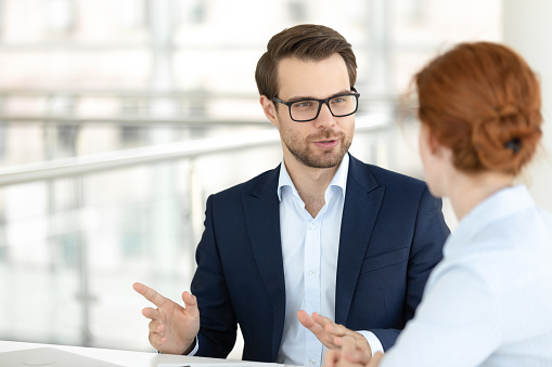 Businessman executive manager explain terms of contract to businesswoman company client partners negotiating sitting at office desk. Partnership mentoring teamwork and vision of future project concept