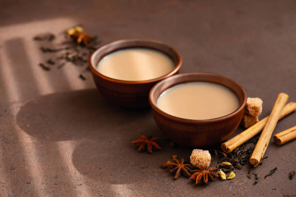 Two cups of spicy Indian masala tea on the table Two cups of spicy Indian masala tea on the brown table, sunny composition Cardamom stock pictures, royalty-free photos & images