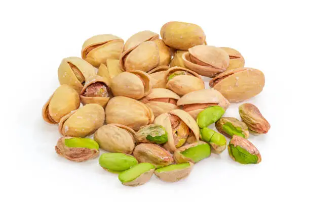 Small pile of the roasted salted pistachio nuts peeled from shells and nuts with partly open shells on a white background
