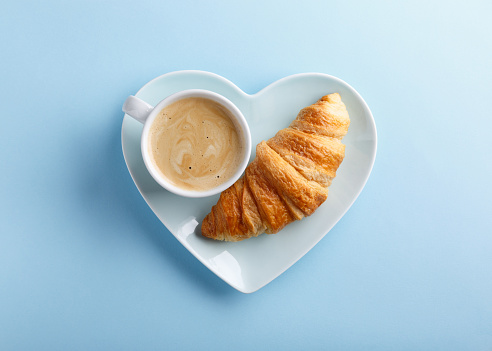 Cup of coffee and freshly baked croissants on blue background. Top view. Copy space.