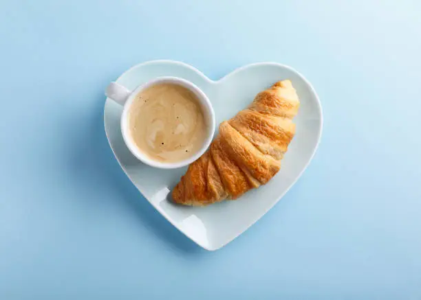 Photo of Cup of coffee and freshly baked croissants on blue background. Top view. Copy space.
