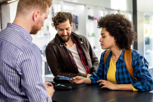 istock Young woman with her partner using a mobile phone virtual wallet application to make a contactless purchase in a store 1139647337