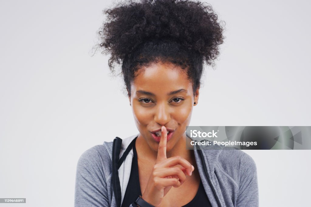 Shhhh don't tell them yet Portrait of an attractive young woman posing with her finger on her lips against a grey background Women Stock Photo
