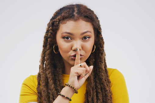 Portrait of an attractive young woman posing with her finger on her lips against a grey background