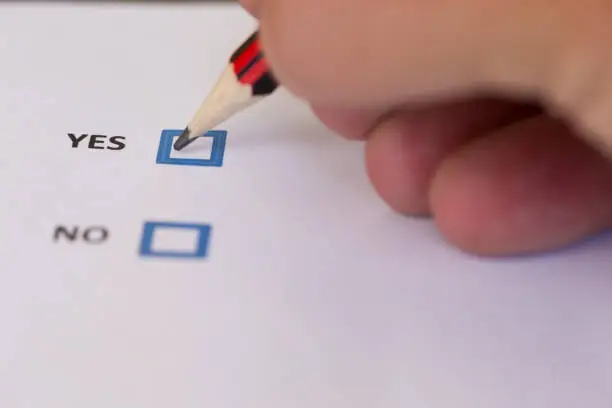 Close up of a hand marking a voting slip with a yes vote.