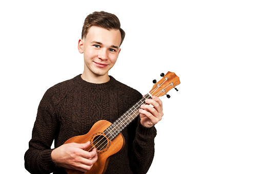 portrait White young guy in sweater play on ukulele in his hands, isolated on a white background.