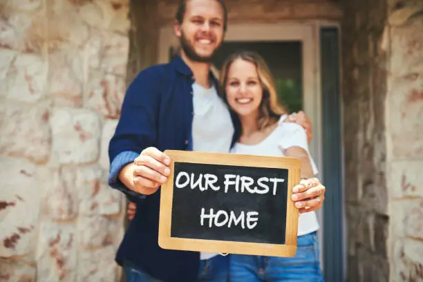 Portrait of a young couple holding a chalkboard with "our first home" written on it