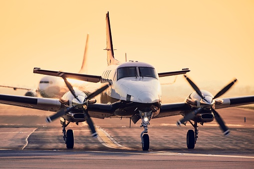 Modern propeller plane against commercial airplane on runway. Traffic at airport during sunset.