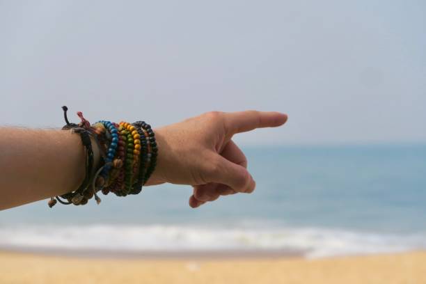 Photo showing beautiful wrist with colourful beaded bracelets against the blue Arabian Sea and Golden Sand in the kerela state of India. These colourful beaded friendship bracelets are dramatic and funky. imagen de muñeca hermosa con coloridas pulseras de abalorios contra el azul del mar arábigo y arena dorada en el estado de kerala de la india. estos coloridos brazaletes de amistad indios son muy dramáticos y funky añadiendo colores a la vida.