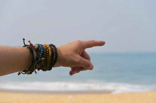 Photo showing beautiful wrist with colourful beaded bracelets against the blue Arabian Sea and Golden Sand in the kerela state of India. These colourful beaded friendship bracelets are dramatic and funky.