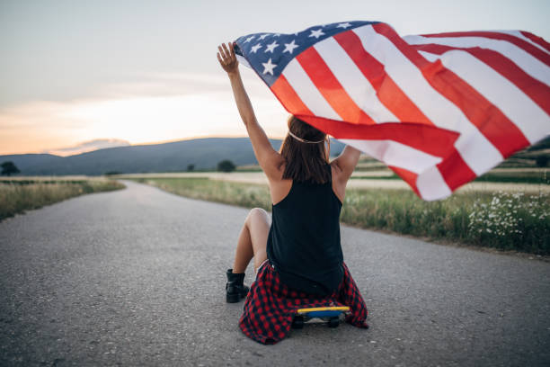 istock Woman sitting on skateboard and holding US flag 1139655975