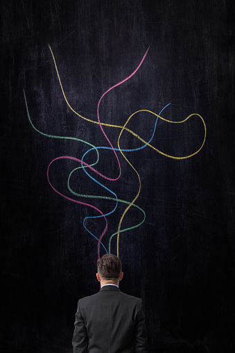 Businessman looking at multicolored lines drawn on blackboard