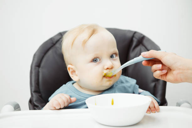 istock Baby in highchair eats cream soup with mothers help 1139668566