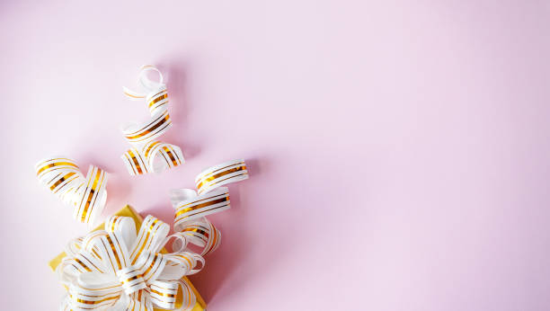 istock Gift box wrapped in white and gold striped ribbon on pastel pink background. Empty note tied over. copy space 1139671349