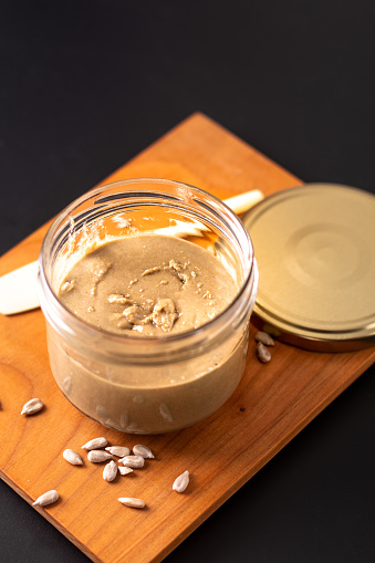 Healthy food concept homemake sunflower butter in glass jar by organic sunflower seeds on black background