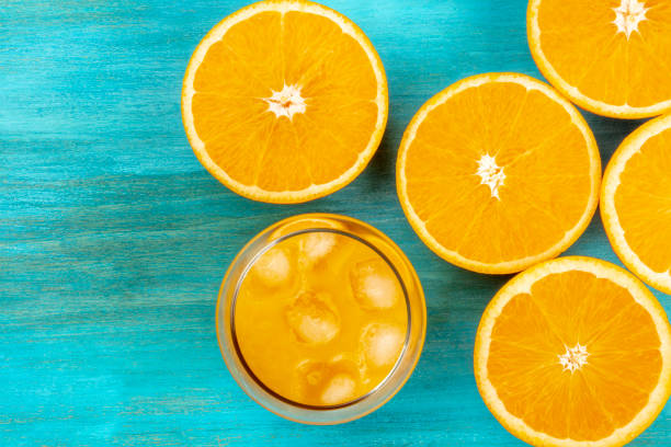 a photo of a glass of fresh orange juice with orange halves, shot from above on a vibrant blue background with a place for text - freshly squeezed orange juice imagens e fotografias de stock