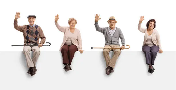 Photo of Senior men and women sitting on a blank billboard sign and waving at the camera