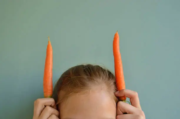 Photo of Girl holding two carrots next to head