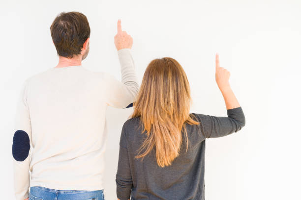 Beautiful middle age couple in love over isolated background Posing backwards pointing behind with finger hand