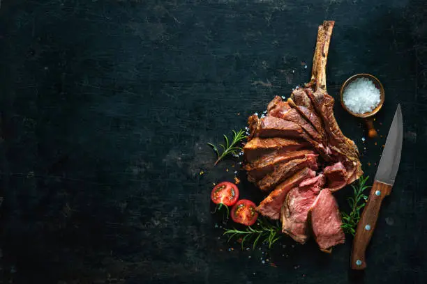 Grilled dry aged tomahawk steak sliced as close-up on dark background