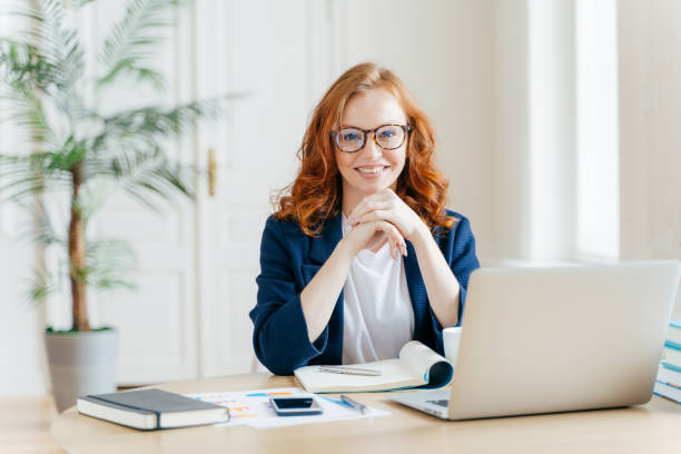 istock Working concept. Intelligent manager with satisfied expression, writes in notepad, works on modern laptop computer, uses organizer app, sits against office interior. Experienced entrepreneur 1139703978