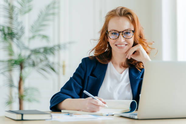 istock Happy successful female writes checklist in notepad, works on creative ideas for startup project, searches necessary information on laptop computer, poses at coworking space, works freelance 1139704003