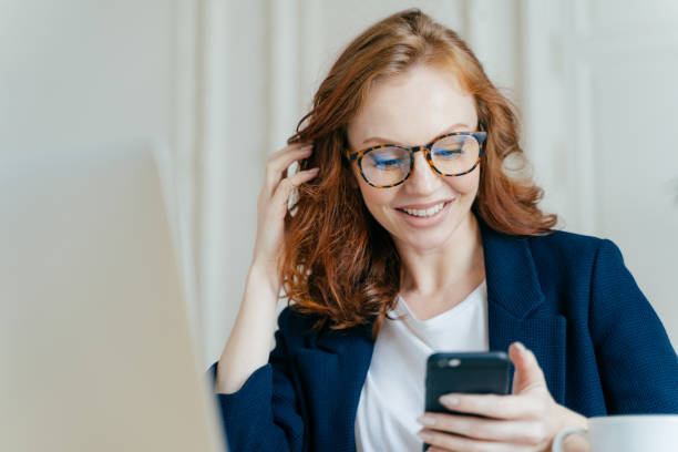 istock Satisfied red haired female uses modern electronic device for checking newsfeed, online communication and searching information, sits in coworking space, uses high speed internet connection. 1139704285