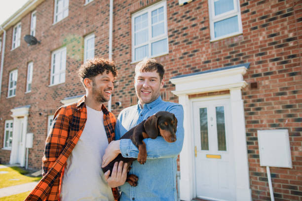 Couple Outside Their New Home A close-up portrait of a caucasian mid-adult man wearing casual clothing, he is smiling and holding his pet sausage dog while standing outside his new home, he is proud and looking at the camera. queer man facing camera stock pictures, royalty-free photos & images