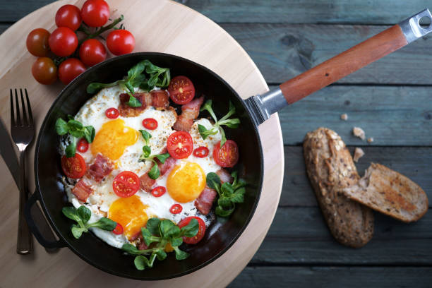istock fried eggs with bacon tomatoes and greens, cast iron pan, top view 1139713272