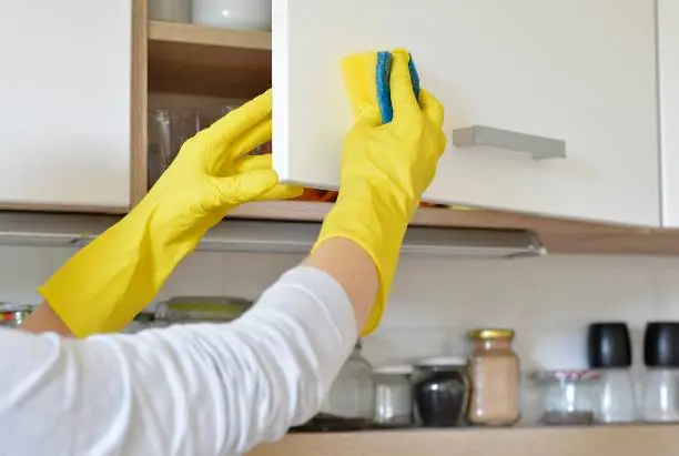 Photo of woman in yellow gloves washes the door in kitchen cabinet