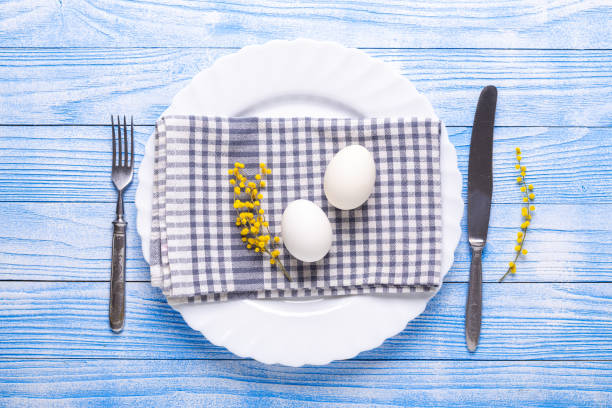 istock Easter table setting. White eggs, napkin on a plate, mimosa flowers, fork, knife on a blue wooden table 1139719735