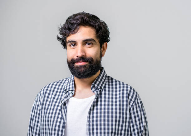 Mid adult man smiling on gray background Portrait of mid adult man smiling on gray background. Handsome male is having beard. Hipster is wearing casuals. black hair stock pictures, royalty-free photos & images