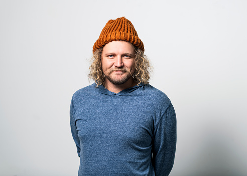 Portrait of young man wearing knit hat on gray background. Handsome male is wearing t-shirt. Hipster is having curly blond hair.