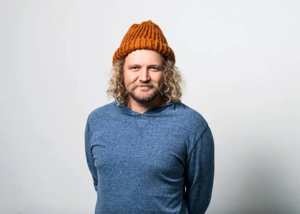 Portrait of young man wearing knit hat on gray background. Handsome male is wearing t-shirt. Hipster is having curly blond hair.