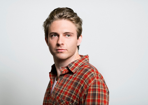 Thoughtful handsome man looking away. Young male is wearing plaid shirt over gray background. Confident hipster is having blond hair.