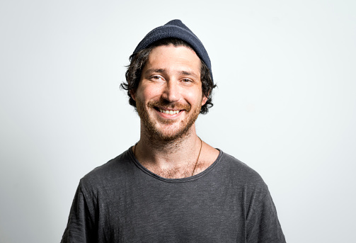 Portrait of mid adult man wearing knit hat and smiling. Handsome male is wearing t-shirt. Hipster is on gray background.