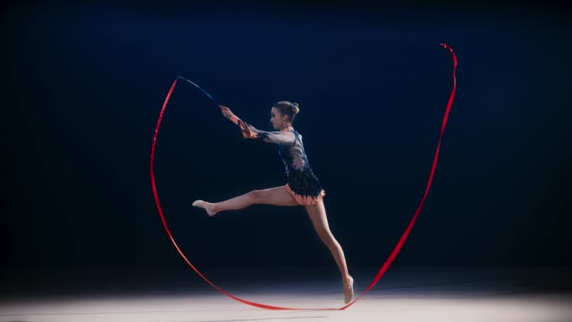 SLO MO LD Rhythmic gymnast doing a split leap while rotating a red ribbon in a wide circle