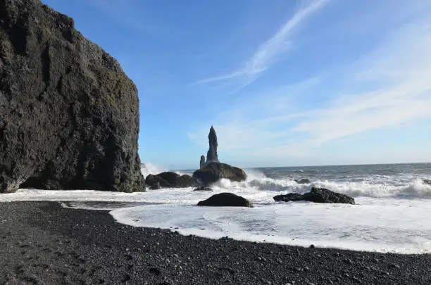 Volcanic black sand beach with waves crashing against them in Iceland.