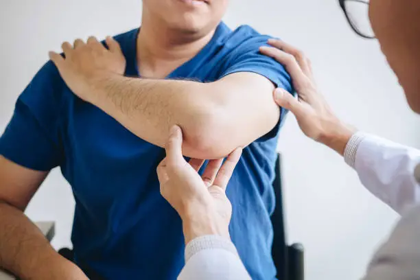 Photo of Doctor physiotherapist assisting a male patient while giving exercising treatment massaging the arm of patient in a physio room, rehabilitation physiotherapy concept