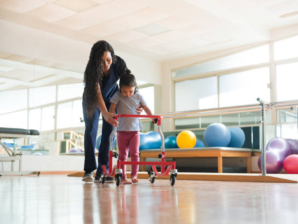 physical therapist helping girl to walk with wheeled frame - child therapy imagens e fotografias de stock