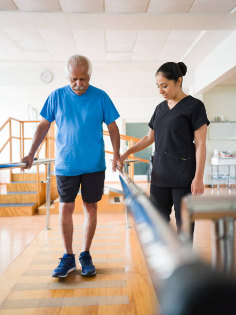 senior man giving small steps between parallel bars - senior adult hospital uniform gray hair imagens e fotografias de stock