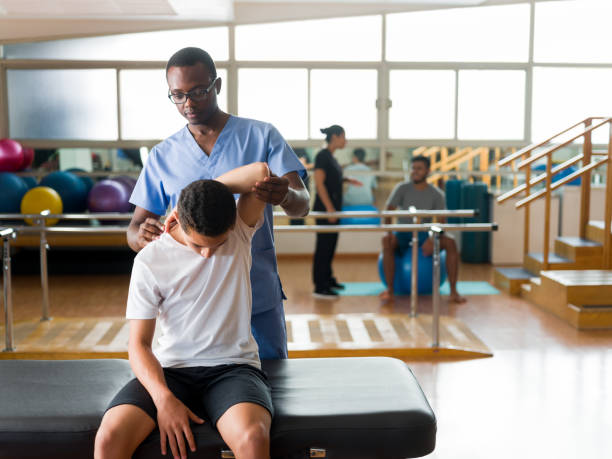 Healthcare provider stretching arm of teenage boy A male healthcare provider stretching the arm of a teenage boy sitting on a massage table. black male massage stock pictures, royalty-free photos & images
