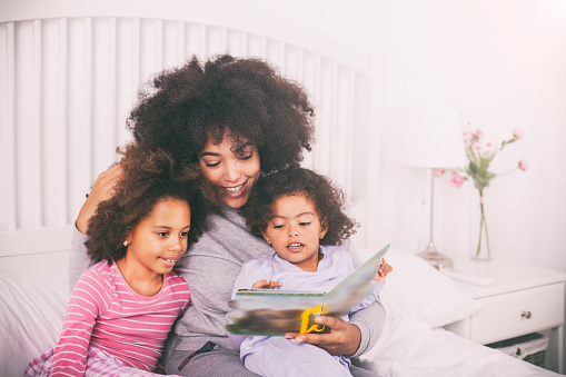 Mother with daughters reading books in bed