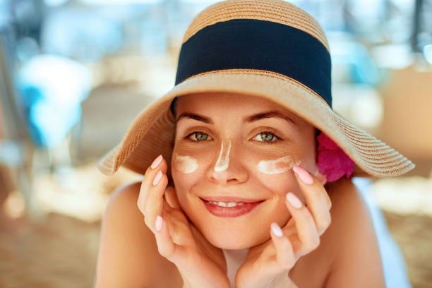 hautpflege. beauty concept. junge hübsche frau, die sonnencreme anwendet und das eigene gesicht berührt. weiblich in hut schmieren sonnencreme lotion auf der haut. hautschutz und dermatologie. - sonnenbaden stock-fotos und bilder