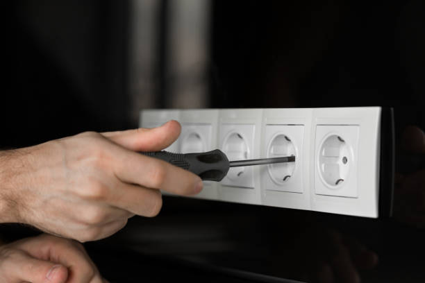 istock Close-up of an electrician's hand with a screwdriver disassembling a white electrical outlet on a black glass wall 1139761886