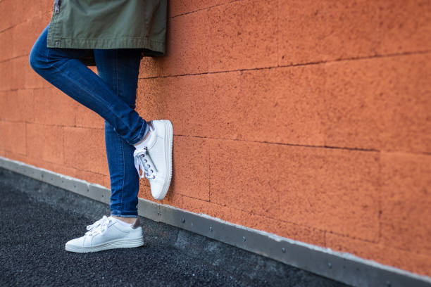스포츠 신발을 가진 여성 다리입니다. 도시에 벽을 기대어 캐주얼 의류와 흰색 운동 화를 입고 여자. - wall women leather street 뉴스 사진 이미지