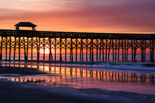 Folly Beach Reflections Sunrise behind the pier at Folly Beach South Carolina in reflected on the wet sand on the beach. charleston south carolina photos stock pictures, royalty-free photos & images