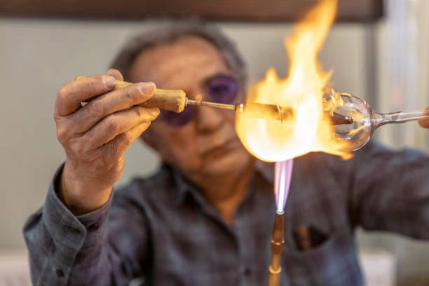 primo piano macro di soffiatore di vetro che lavora con fiamma su un bicchiere da vino fatto a mano da cristallo prezioso in un laboratorio. concetto di fatto a mano, di alta qualità, artigianale, made in istanbul, turchia, soffiatura del vetro. - glass blower foto e immagini stock