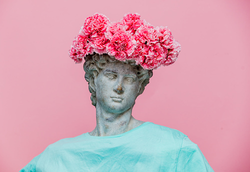 Antique bust of male with carnations bouquet in a hat on pink background. Ready for summer vacation