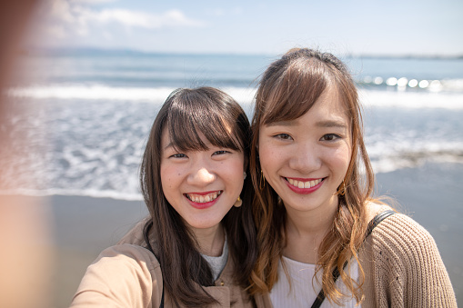 Young female friends taking selfie pictures in front of Pacific Ocean